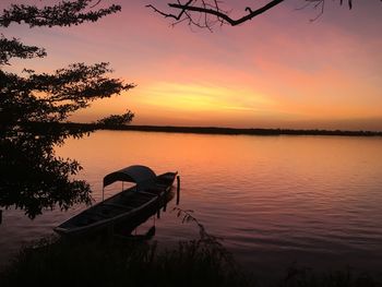 Silhouette tree by lake against orange sky