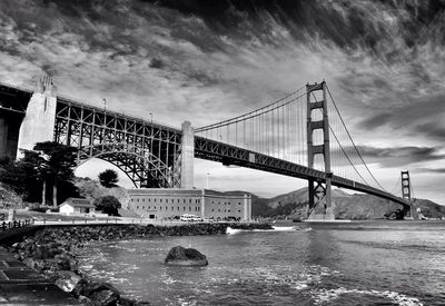 Low angle view of bridge over river against cloudy sky