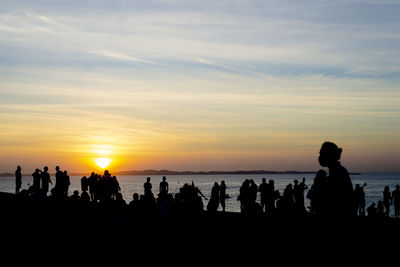 Silhouette people at beach against sky during sunset