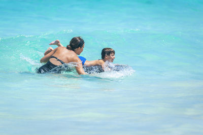 Woman assisting son surfboarding in sea