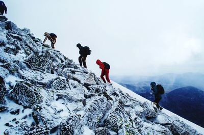 People skiing on snowcapped mountains against cloudy sky