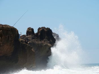 Sea waves splashing on rocks against clear sky