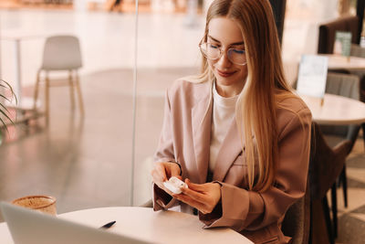 A millennial business woman in glasses and casual clothes hold headphones in hands in coffee shop