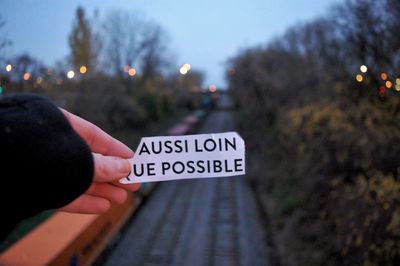 Close-up of hand holding text against railroad tracks