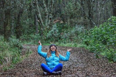 Full length of smiling woman sitting on land in forest