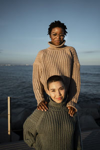 Smiling woman standing behind friend against sky