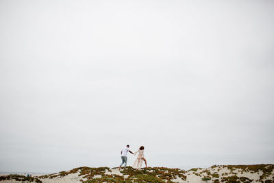 Mixed race couple climbing sand dunes for maternity photos
