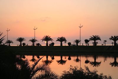 Silhouette palm trees by lake against sky during sunset