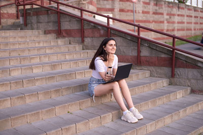 Full length of young woman sitting on staircase