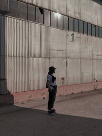 Full length of man standing on footpath against wall