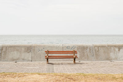 Empty bench by sea against sky