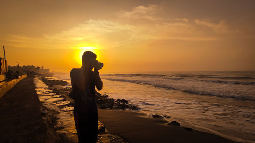 Woman standing on beach against sky during sunset