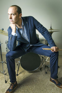 Confident drummer sitting on drum against wall