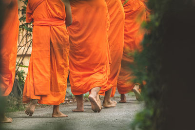 Low section of people wearing orange traditional clothing while walking on road