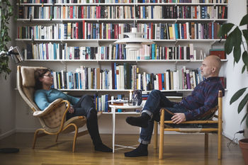 Full length of therapist and patient discussing by bookshelf at home office