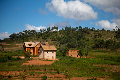 House on field by trees against sky