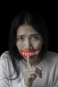 Portrait of sad woman with duct tape on mouth against black background