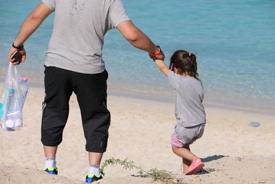 Rear view of father and daughter holding hands while walking at beach