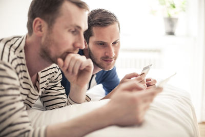 Homosexual couple looking at credit card while lying in bed at home