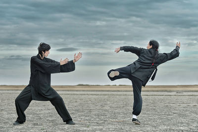 People practicing martial arts on land against cloudy sky