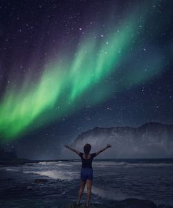 Rear view of woman standing by sea against sky at night