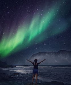 Rear view of man standing in sea against sky at night