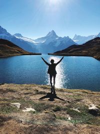 Rear view of woman standing with arms outstretched by lake against sky