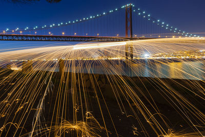 Illuminated wire wool by lake against sky at night