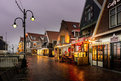 Illuminated street amidst buildings against sky at dusk