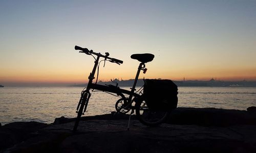 Silhouette bicycle on beach against clear sky during sunset