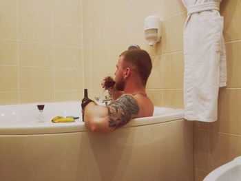 Side view of man drinking wine while relaxing in bathtub