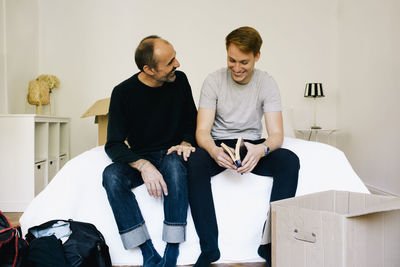 Happy parent talking with son while sitting on bed at home