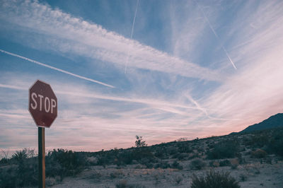 Road sign by landscape against sky