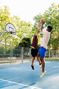 Ethnic african american friends players running together with ball while playing basketball on sports ground in sunny day