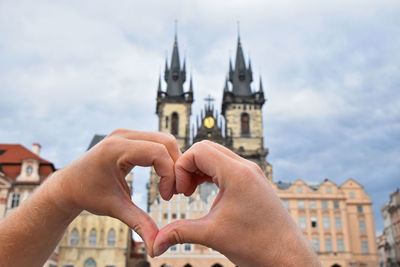 Cropped image of person making heart shape with hands against building in city
