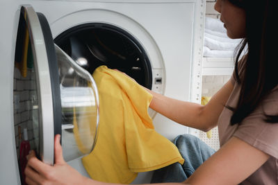 Midsection of woman washing clothes in machine at home