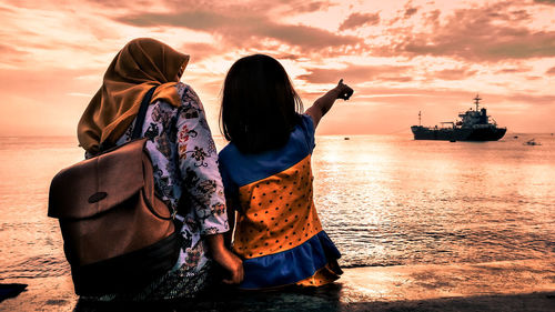 Rear view of people on beach against sky during sunset