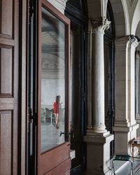 Women in red dress reflected in windows of historic building.