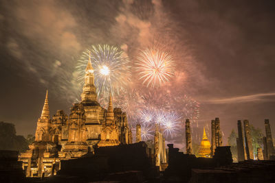 Firework display by illuminated building against sky at night