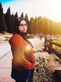 Portrait of young woman standing on road against sky in park during winter