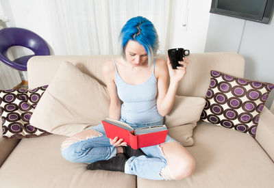 High angle view of woman reading book while sitting on sofa at home