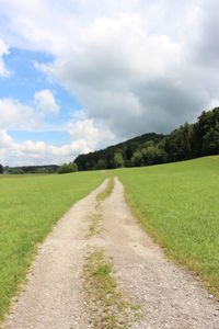 Dirt road amidst field against sky