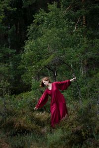 Woman wearing red dress standing on land in forest