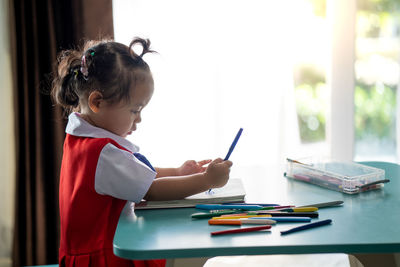 Side view of girl drawing in book at table