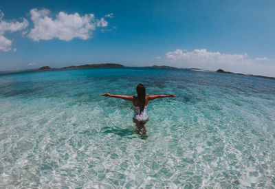 Rear view of woman with arms outstretched standing in sea