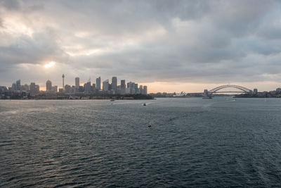 Sea by buildings against sky during sunset