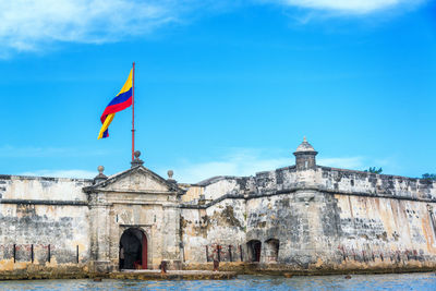 Colombian flag on historic fort by sea against sky