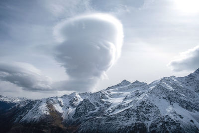 Mountain range, steep snow-covered rocky slopes and peaks and large bizarre cloud. selective focus.