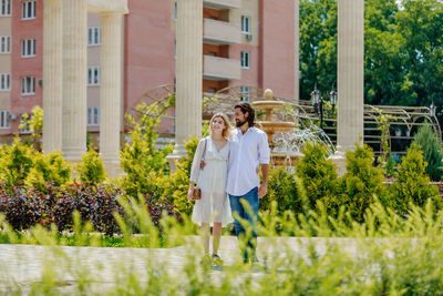 Couple walking on footpath amidst plants against building