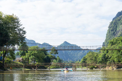 People on bridge over river against sky